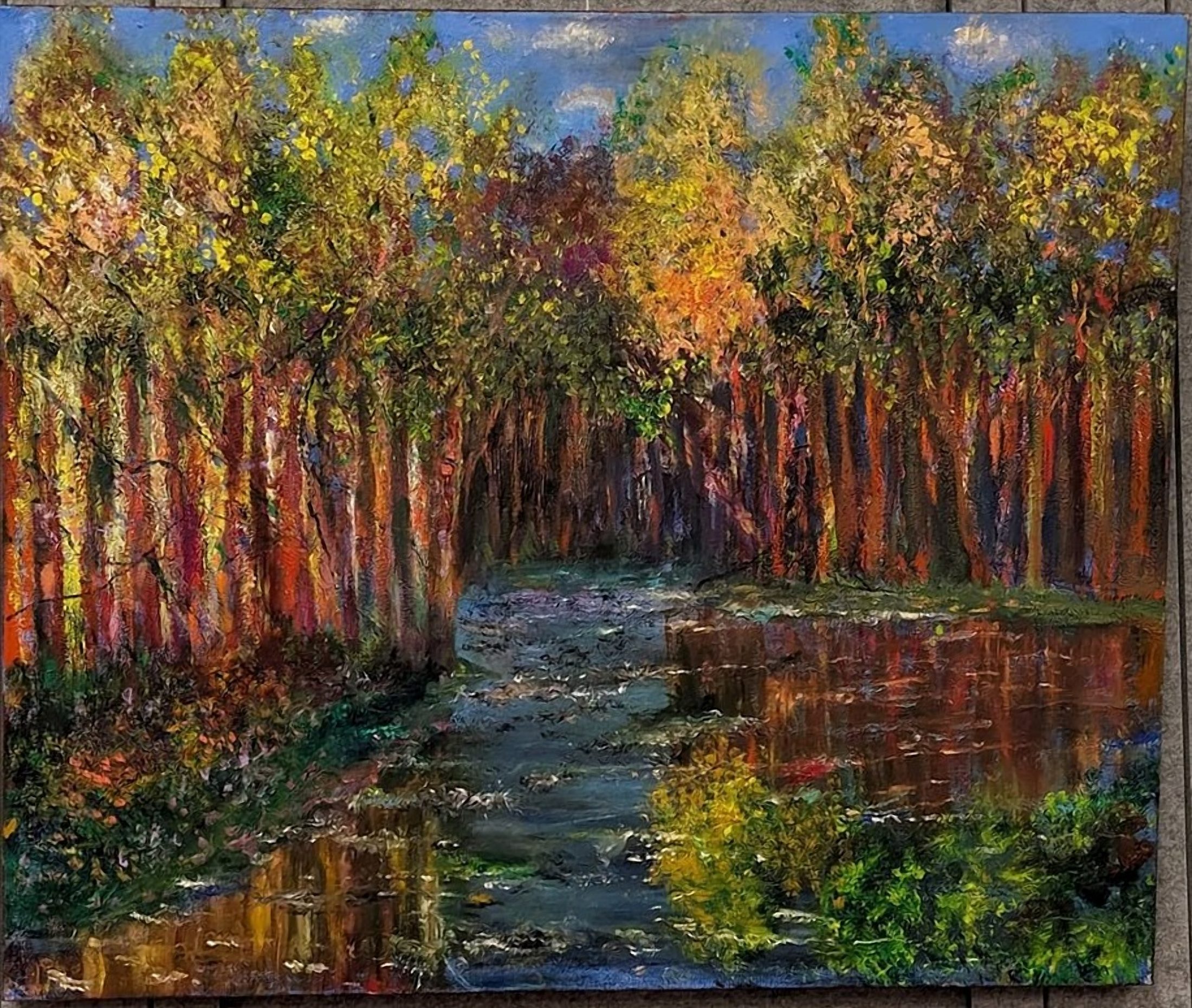 Reflections in Red Woods. A creek winds between tall autumn trees with red and gold trunks, the water mirroring the canopy in ripples of orange, green and blue.