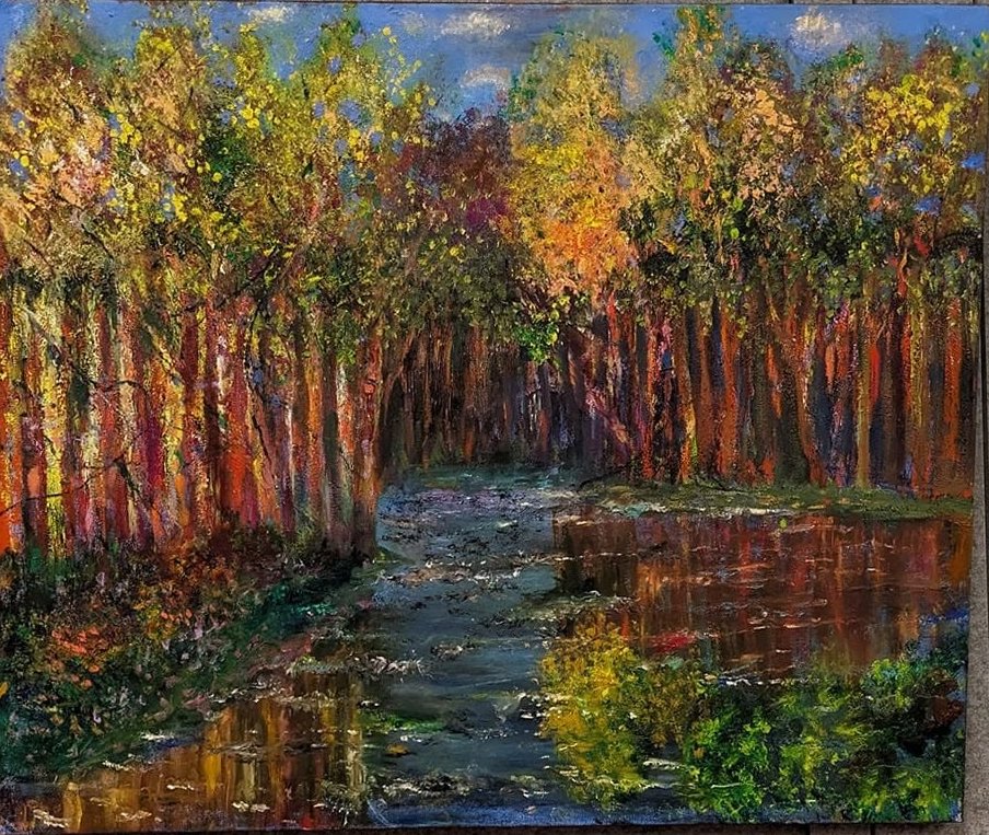 Reflections in Red Woods. A creek winds between tall autumn trees with red and gold trunks, the water mirroring the canopy in ripples of orange, green and blue.